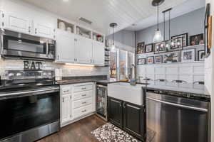Kitchen featuring stainless steel appliances, white cabinets, dark cabinetry, dark stone counters, and wooden ceiling
