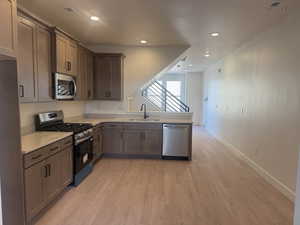 Kitchen featuring appliances with stainless steel finishes, light wood-type flooring, recessed lighting, a peninsula, and light stone countertops