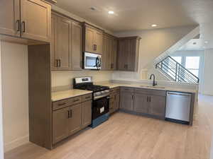 Kitchen with stainless steel appliances, light wood-type flooring, recessed lighting, and light stone counters