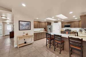 Kitchen with a breakfast bar, a skylight, light stone counters, appliances with stainless steel finishes, and a peninsula