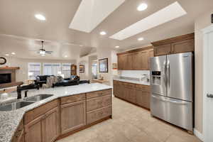 Kitchen with stainless steel fridge with ice dispenser, brown cabinets, light stone counters, a skylight, and open floor plan