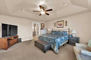 Bedroom featuring a raised ceiling, light carpet, and ceiling fan