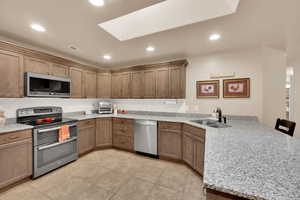Kitchen featuring appliances with stainless steel finishes, light stone counters, a peninsula, a skylight, and a breakfast bar
