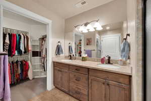 Full bathroom with double vanity, a walk in closet, light tile patterned floors, and light carpet