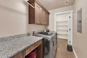 Washroom featuring light tile patterned flooring, cabinet space, electric panel, and washing machine and clothes dryer