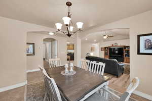 Dining area with arched walkways, vaulted ceiling, a chandelier, ceiling fan, and light tile patterned floors