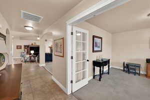 Corridor with arched walkways, light tile patterned flooring, light colored carpet, and vaulted ceiling
