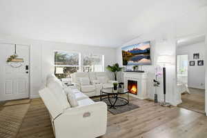 Living area featuring a warm lit fireplace, vaulted ceiling, wood finished floors, and a textured ceiling