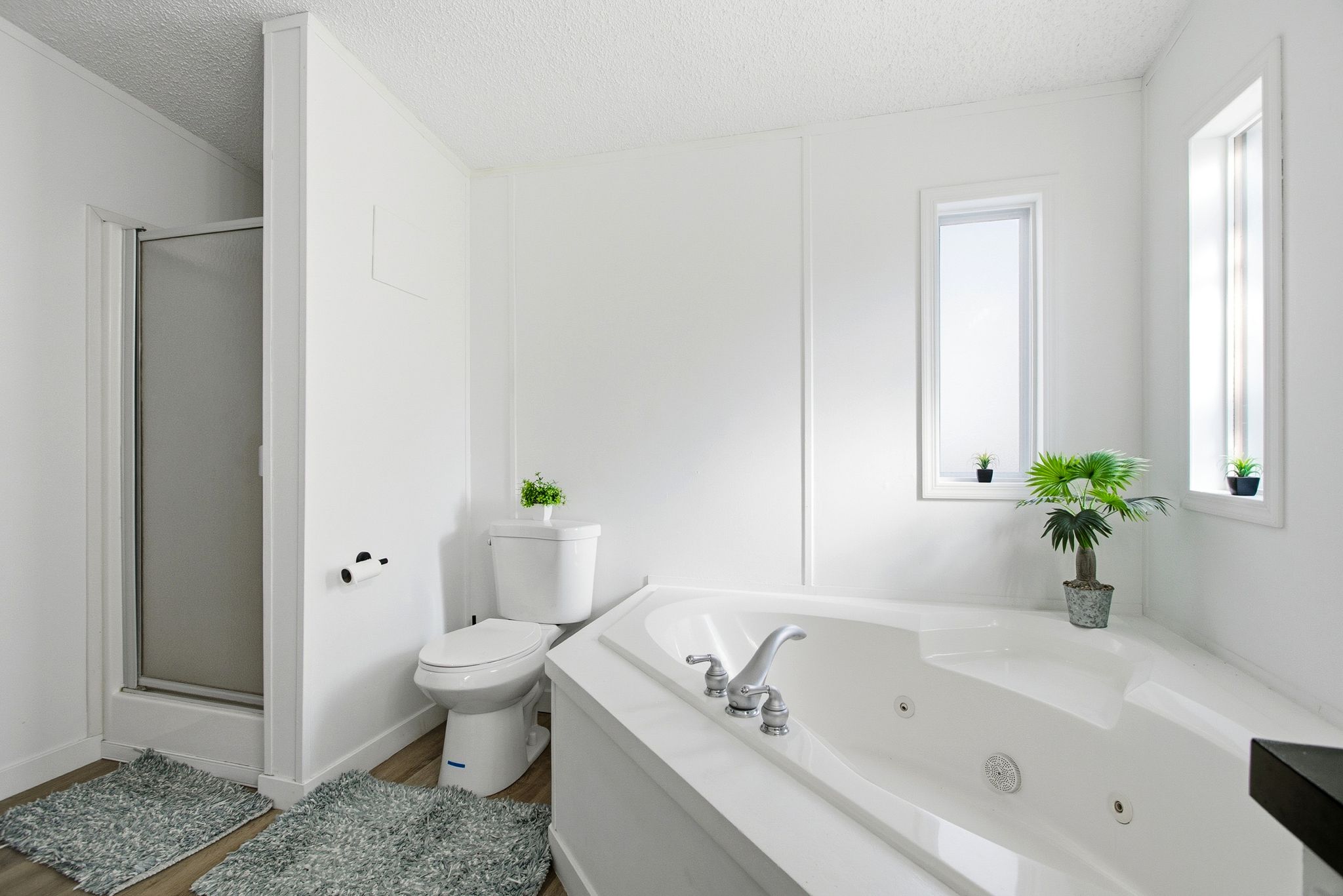 Full bath featuring a stall shower, a tub with jets, a textured ceiling, and wood finished floors