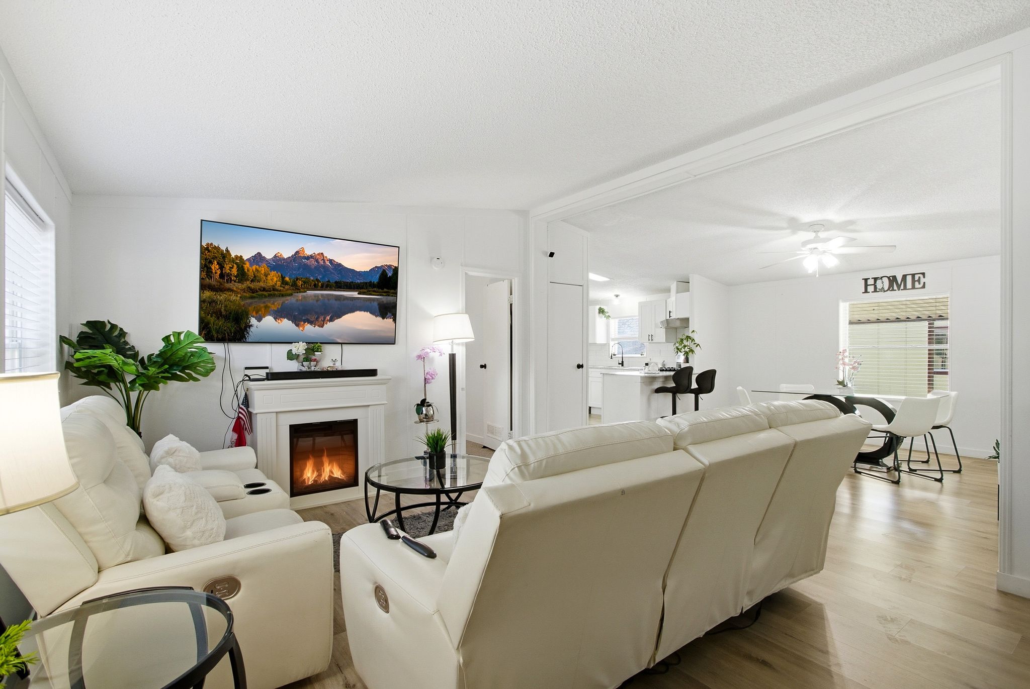Living area featuring lofted ceiling, wood finished floors, a glass covered fireplace, ceiling fan, and a textured ceiling