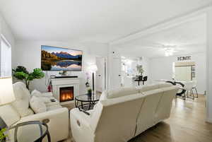 Living area featuring lofted ceiling, wood finished floors, a glass covered fireplace, ceiling fan, and a textured ceiling