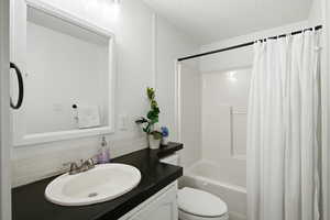 Full bathroom featuring a textured ceiling, vanity, shower / bath combination with curtain, and backsplash