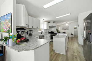 Kitchen with white cabinets, appliances with stainless steel finishes, light wood-style floors, a peninsula, and a center island