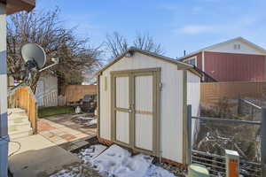 Snow covered structure with a fenced backyard and a storage shed