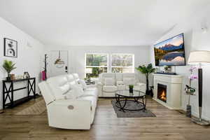 Living area featuring a warm lit fireplace, wood finished floors, a textured ceiling, and ornamental molding