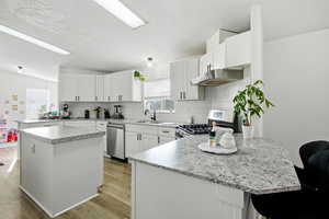 Kitchen with a peninsula, a breakfast bar, appliances with stainless steel finishes, white cabinets, and a textured ceiling