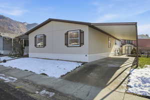 View of snow covered exterior featuring driveway, a carport, and an outbuilding
