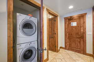 Laundry area with stone tile floors, estacked washer and dryer, and recessed lighting