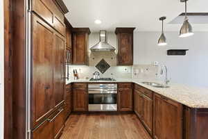 Kitchen featuring a peninsula, stainless steel oven, light stone countertops, wall chimney exhaust hood, and decorative light fixtures