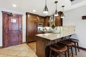Kitchen with inlaid floor details, a kitchen bar, light stone countertops, a peninsula, and hanging light fixtures