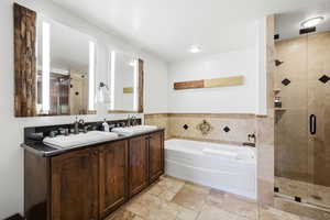 Bathroom with a garden tub, double vanity, a stall shower, and stone tile floors