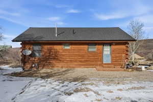 Snow covered back of property with log siding and a shingled roof
