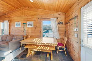 Dining space featuring vaulted ceiling, wooden ceiling, wood walls, and stone finish flooring
