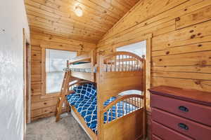 Carpeted bedroom featuring wooden walls, lofted ceiling, and wood ceiling