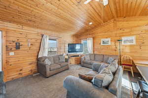 Living area with wooden ceiling, vaulted ceiling, carpet flooring, and wood walls