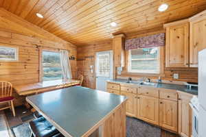 Kitchen with wooden ceiling, vaulted ceiling, wooden walls, light brown cabinetry, and white appliances