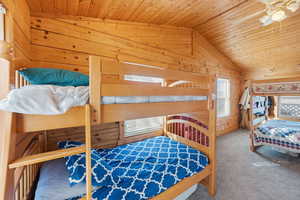 Bedroom featuring wooden walls, wood ceiling, carpet, vaulted ceiling, and ceiling fan