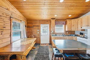 Kitchen featuring lofted ceiling, wooden ceiling, light brown cabinets, white range with gas stovetop, and stone tile flooring