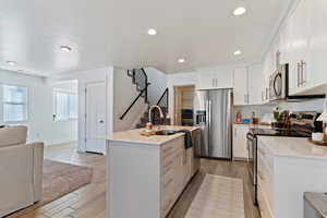 Kitchen featuring appliances with stainless steel finishes, open floor plan, a center island with sink, light wood-style flooring, and light stone counters