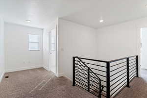 Hall with carpet flooring, an upstairs landing, and a textured ceiling