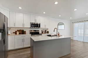 Kitchen with white cabinetry, stainless steel appliances, an island with sink, light stone counters, and recessed lighting