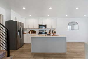 Kitchen featuring appliances with stainless steel finishes, white cabinetry, an island with sink, wood finish floors, and recessed lighting