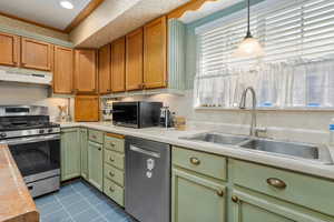 Kitchen with stainless steel appliances, light countertops, green cabinets, and under cabinet range hood
