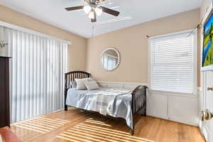 Bedroom with a decorative wall, a wainscoted wall, light wood-style flooring, and ceiling fan