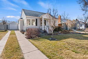 Bungalow featuring an outbuilding, a front lawn, driveway, a detached garage, and a shingled roof