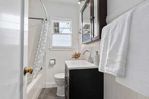 Full bath featuring vanity, shower / bath combo with shower curtain, dark wood-style flooring, and wainscoting