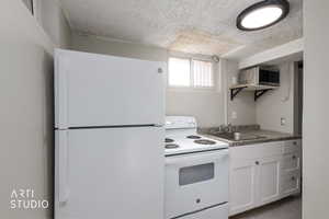 Kitchen featuring white appliances, open shelves, white cabinetry, dark countertops, and a textured ceiling