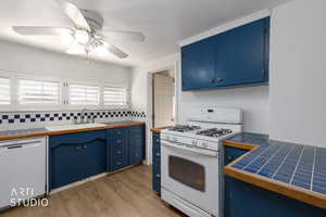 Kitchen featuring tile countertops, blue cabinetry, white appliances, light wood-style flooring, and tasteful backsplash