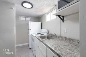 Kitchen featuring white appliances, light countertops, light tile patterned flooring, white cabinetry, and a textured ceiling