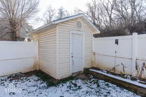 Snow covered structure featuring a storage shed and a fenced backyard