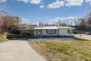 Ranch-style home with covered porch, a front yard, a carport, driveway, and a chimney