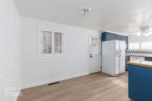 Kitchen with blue cabinetry, white appliances, light wood-type flooring, a ceiling fan, and backsplash
