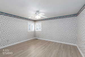 Empty room featuring light wood-style floors, wallpapered walls, and ceiling fan
