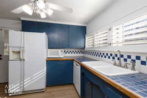 Kitchen featuring blue cabinets, white appliances, tile counters, light wood-style flooring, and backsplash