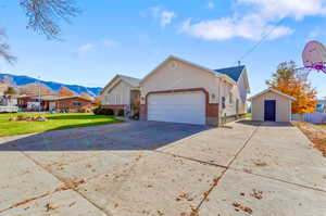 View of front of property featuring driveway, a front yard, a mountain view, an outbuilding, and stucco siding