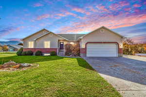 Ranch-style house with brick siding, concrete driveway, a yard, a garage, and stucco siding